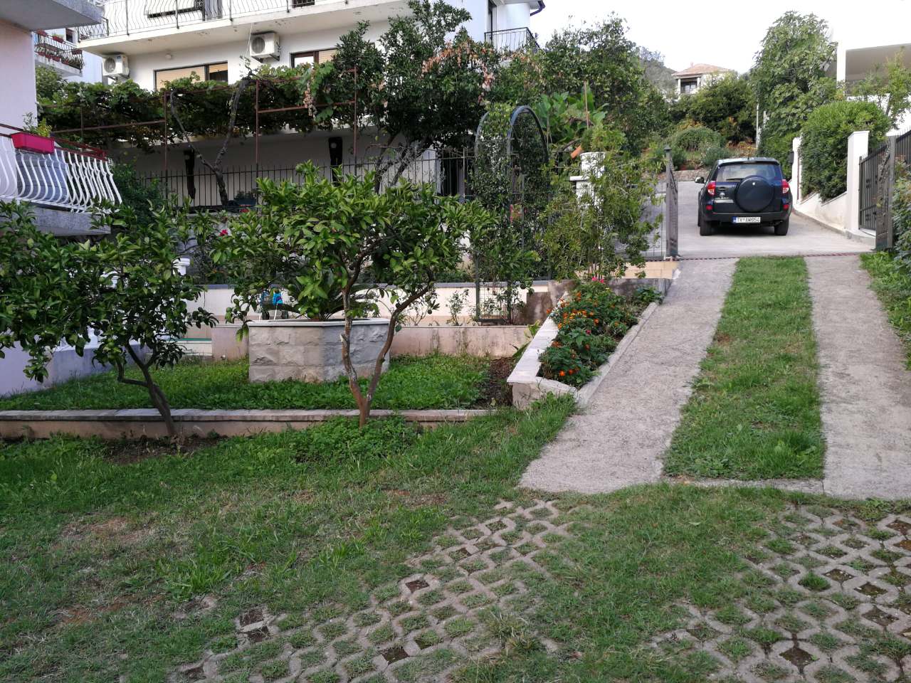 Courtyard of a private house in Tivat, Montenegro: a green garden, parking space, and a view of the building facade.