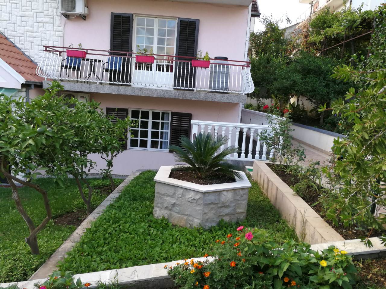 Two-story house in Tivat, Montenegro, with a cozy garden, terrace, stone flower bed, and greenery.
