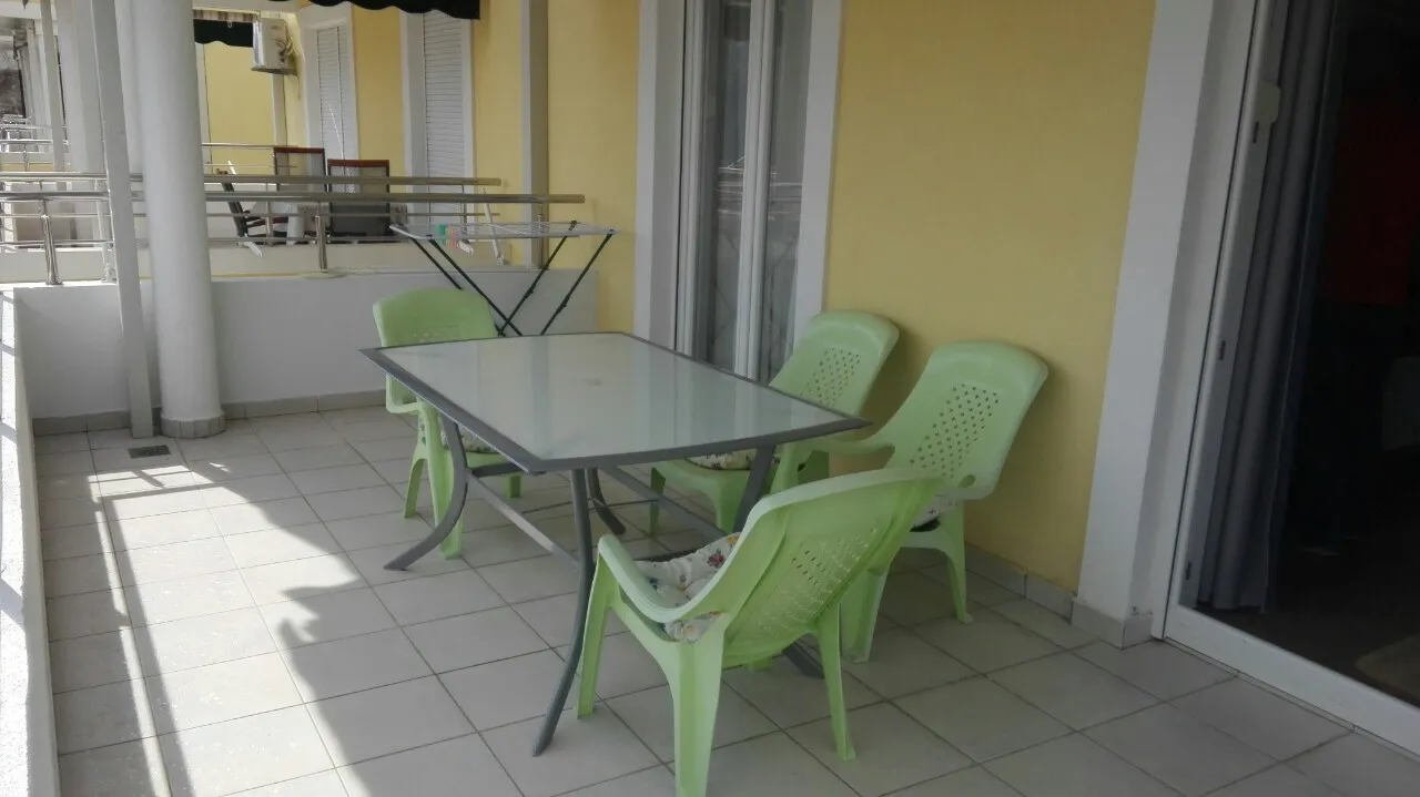 Balcony with green plastic chairs and glass table against a yellow wall.