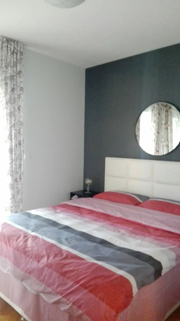 Bed with striped bedding against a dark gray wall featuring a round mirror and floral curtains.