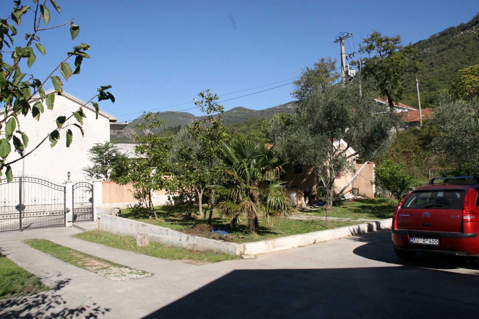 View of the villa’s grounds in Kavači, Bay of Kotor, Montenegro: a garden with palm trees and parking by the house.