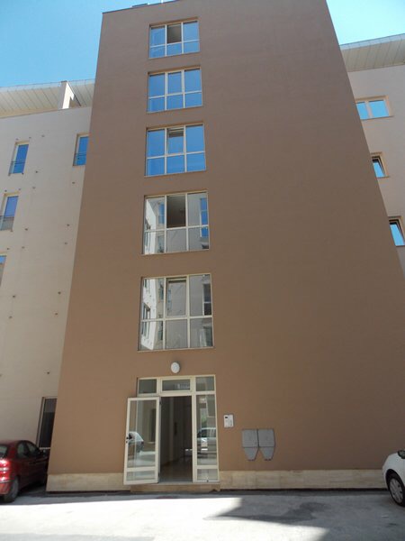 Facade of a modern apartment building in Budva, Montenegro: beige walls, panoramic windows, and entrance area.