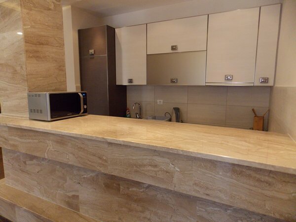 Modern kitchen with a marble bar counter in an apartment in Budva, Montenegro: white cabinets and built-in appliances.