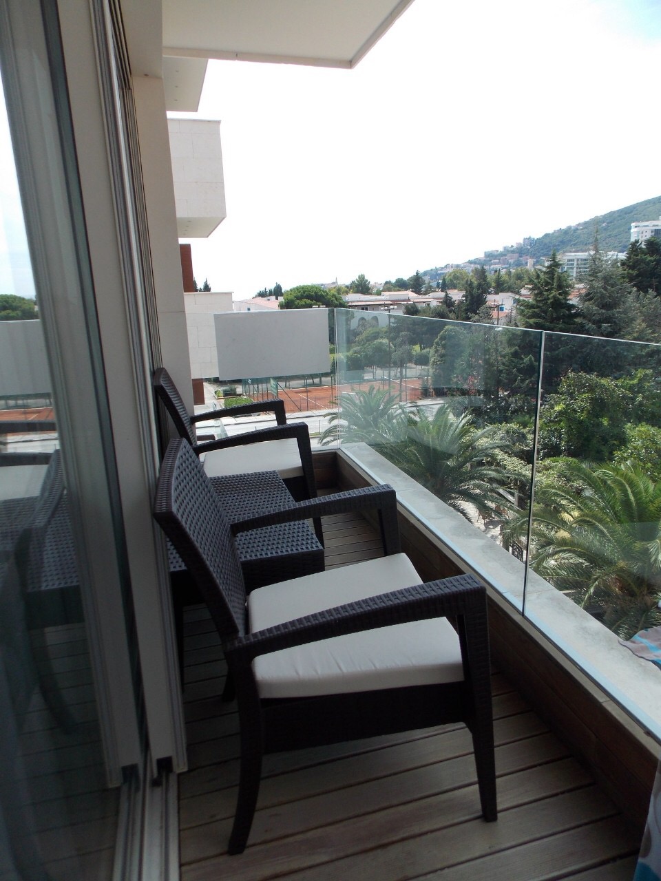 Balcony with wicker furniture in an apartment in Budva, Montenegro, overlooking a green park and tennis courts.