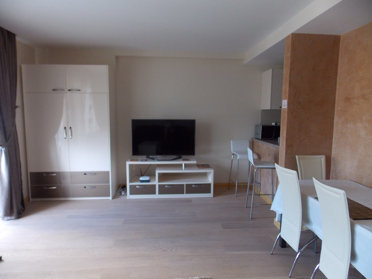 Living room with dining area in an apartment in Budva, Montenegro: light furniture, TV area, bar counter, and parquet flooring.