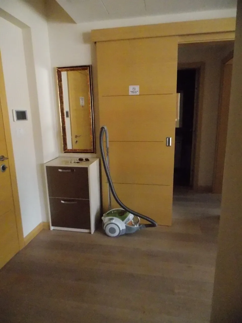 Hallway with a wooden sliding door, wall mirror, small cabinet, and a vacuum cleaner on the floor.