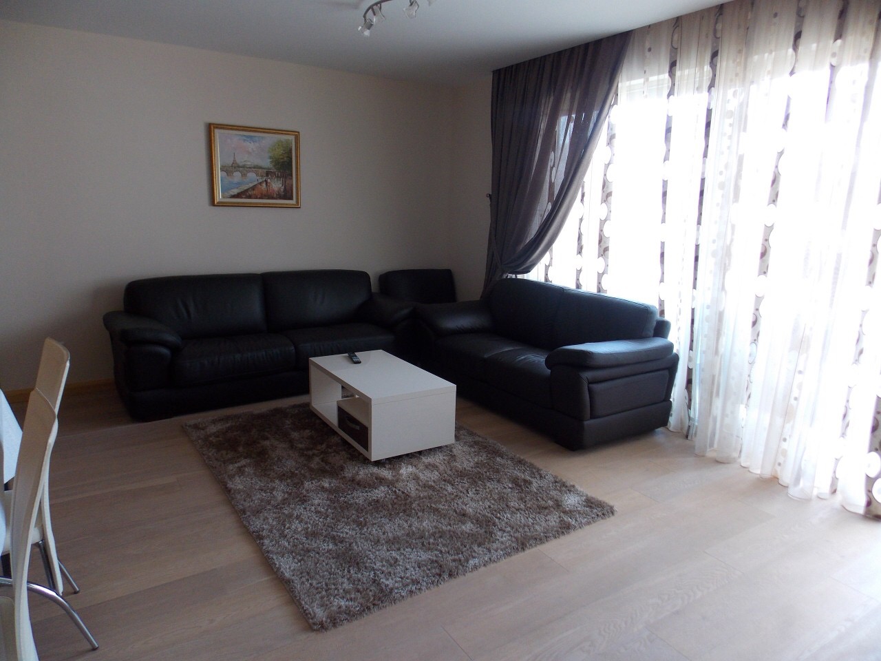 Living room in an apartment in Budva, Montenegro: leather sofas, a white coffee table, and panoramic windows with sheer curtains.