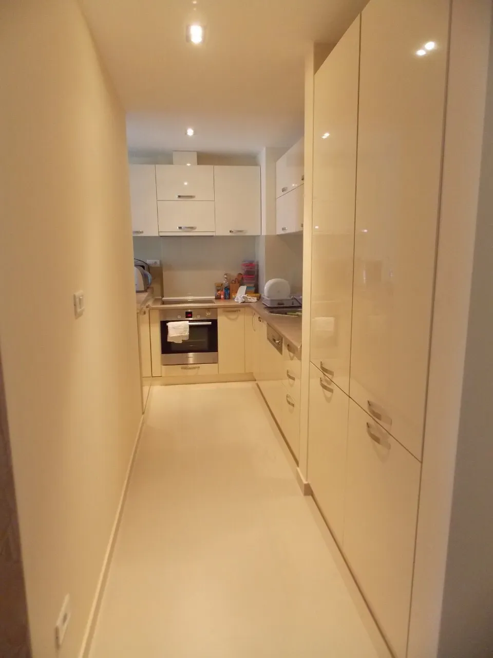 Narrow kitchen with glossy white cabinets, built-in oven, and dishwasher visible along the counter.