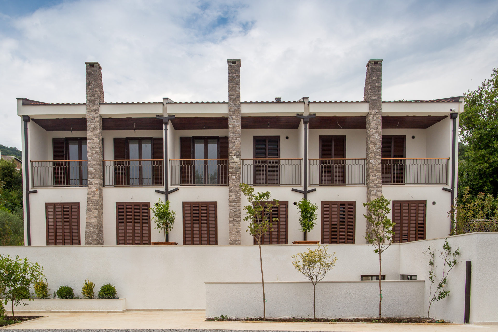 Facade of a modern residential complex in Tivat, Montenegro: white walls, stone columns, and wooden shutters on the windows.