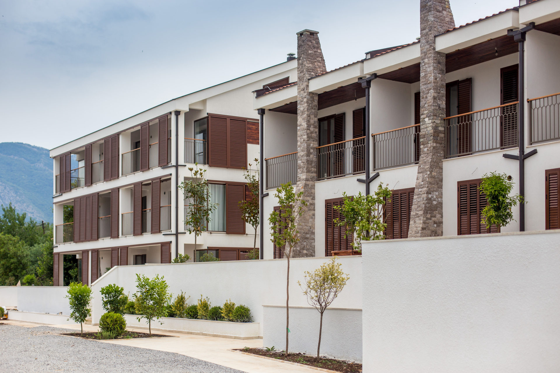 Modern residential complex in Tivat, Montenegro: white facades, balconies with stone finishes, and green landscaping.