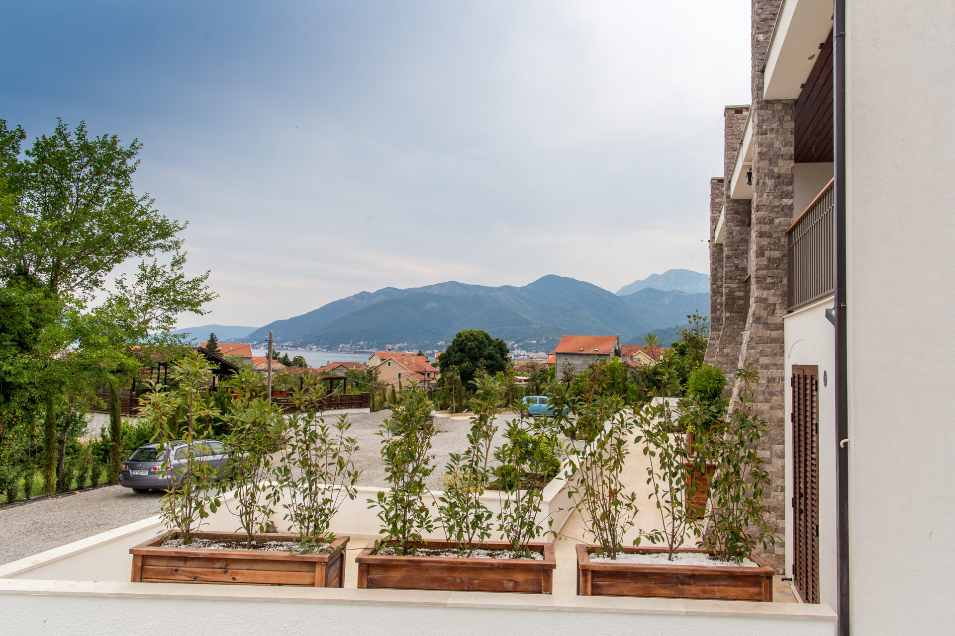 View from the balcony of a modern apartment in Tivat, Montenegro: stone facade, greenery, and mountains.
