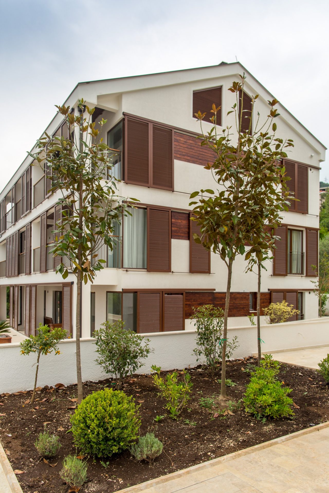Modern residential building with terraces and wooden shutters in Tivat, Montenegro, surrounded by a well-kept garden.