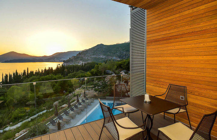 Apartment balcony in Kamenovo, Montenegro: sea, mountain, and pool view, wooden finish, table with chairs.