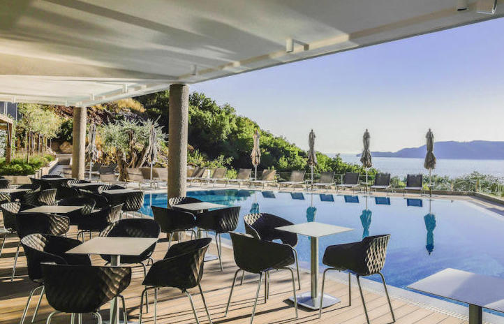 Open terrace with a pool and sea view in Kamenovo, Montenegro: tables, wicker chairs, and sun loungers by the water.