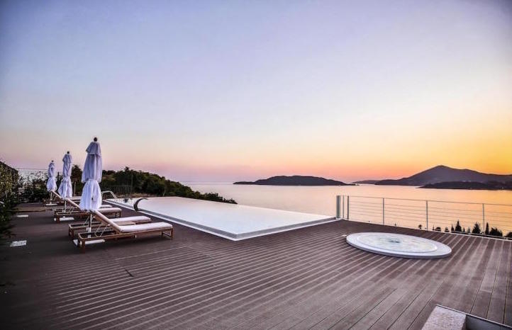 Terrace with infinity pool, jacuzzi, and sea view in Kamenovo, Montenegro: sun loungers and lounge area at sunset.