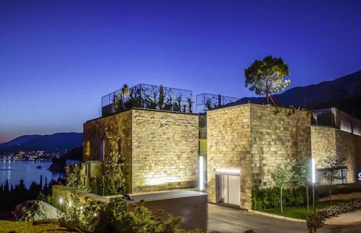 Modern villa with a stone facade and rooftop terrace in Kamenovo, Montenegro, sea view at dusk.