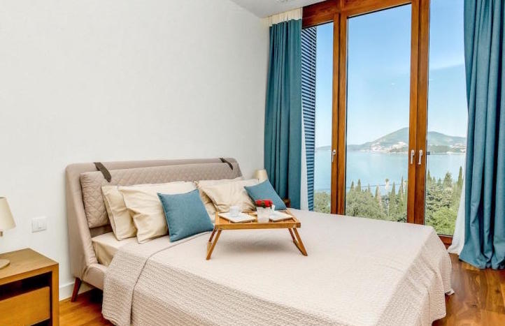 Bedroom in an apartment in Kamenovo, Montenegro: double bed, panoramic windows with sea and mountain views.