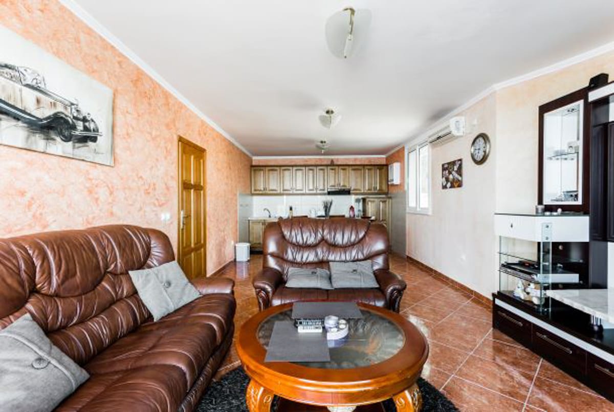 Living room with leather sofas and a kitchen in a house in Kruče, Montenegro: interior with tile and wooden furniture.
