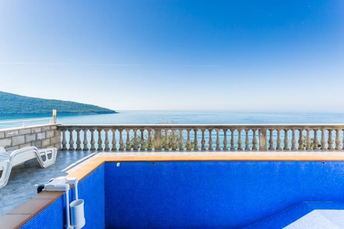 Open-air pool with sea and mountain views by the house in Kruče, Montenegro: terrace with sun loungers and a stone balustrade.
