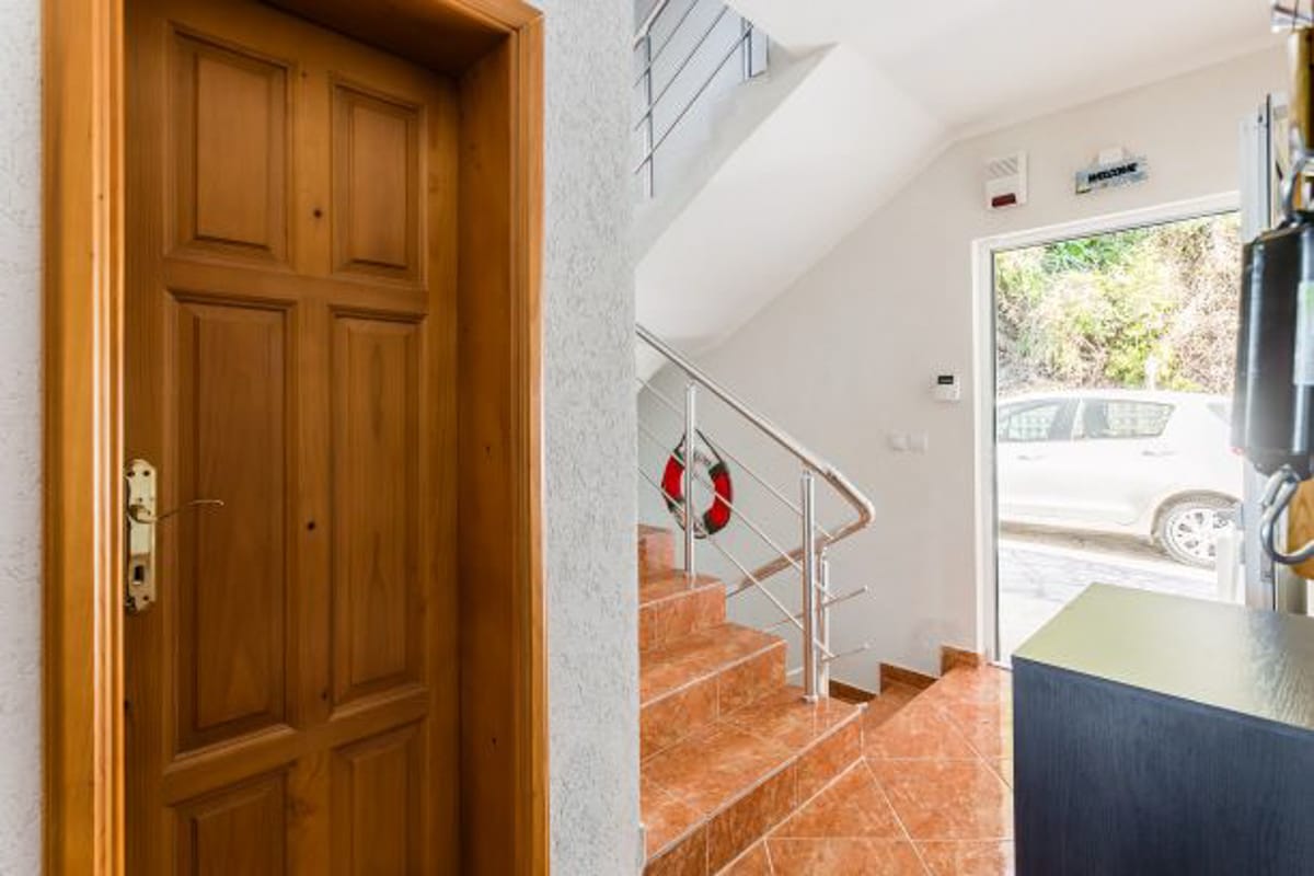 Hallway with a wooden door and staircase in a house in Kruče, Montenegro: tiled floor, metal railings, and a view of the street.