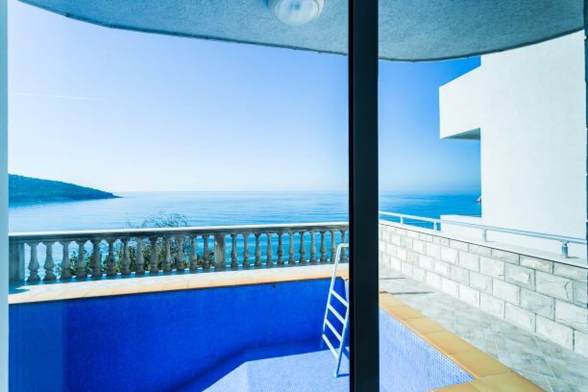 Terrace with a pool and panoramic sea view in a house in Krucha, Montenegro: tiled finish and stone railings.