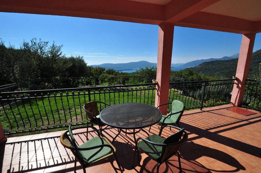 Terrace with black metal table and green chairs overlooking a lake and mountains.