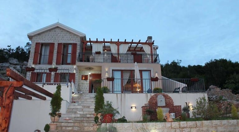 Two-story stone villa with a terrace and pergola in Krimovica, Montenegro: front view with staircase and garden.
