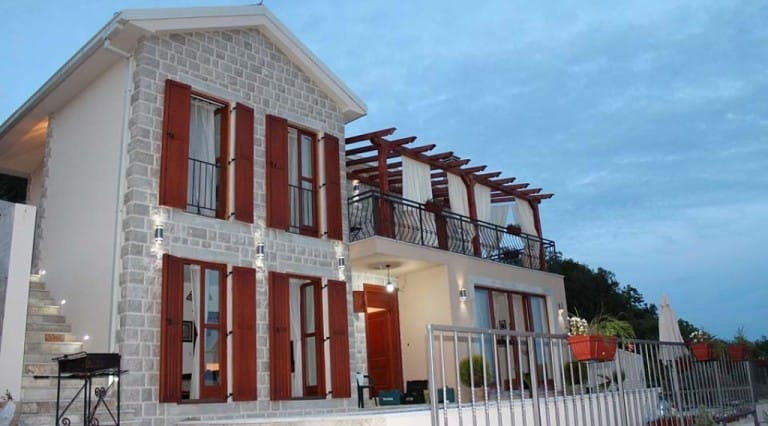 Two-story stone villa with a terrace and wooden shutters in Krimovica, Montenegro, exterior view at evening.