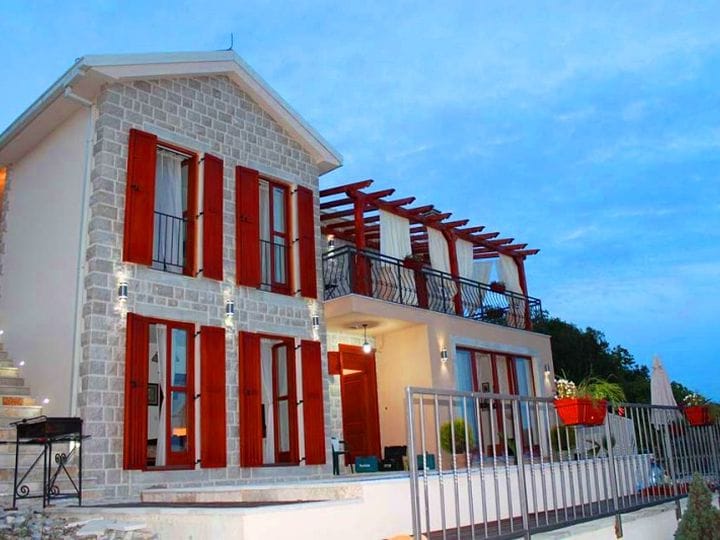 Two-story villa in Krimovica, Montenegro: stone facade, red shutters, and a terrace with a wooden pergola.