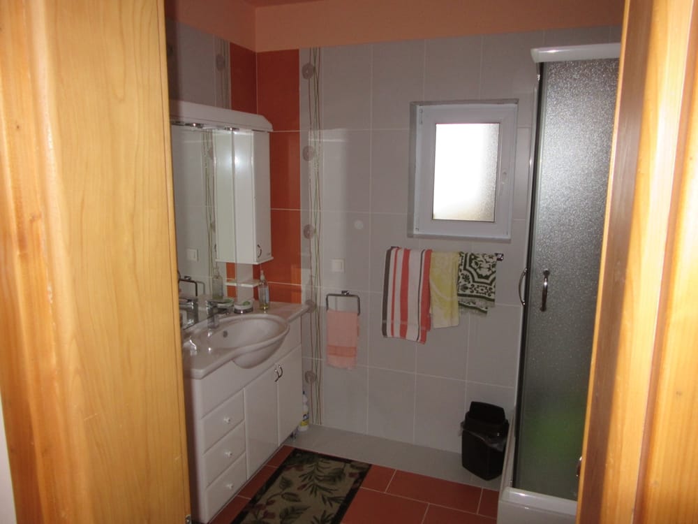 Bathroom with shower cabin and vanity in a villa, Reževići, Montenegro. Light tiles, window, and sanitary ware.