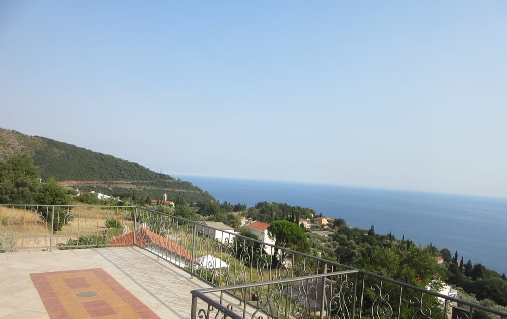 Panoramic sea and mountain view from the villa terrace in Reževići, Montenegro: tiled floor and wrought-iron balcony railings.
