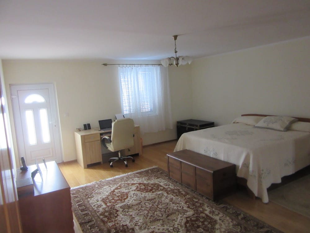 Spacious bedroom with a double bed and workspace in a villa in Reževići, Montenegro, with wooden flooring.
