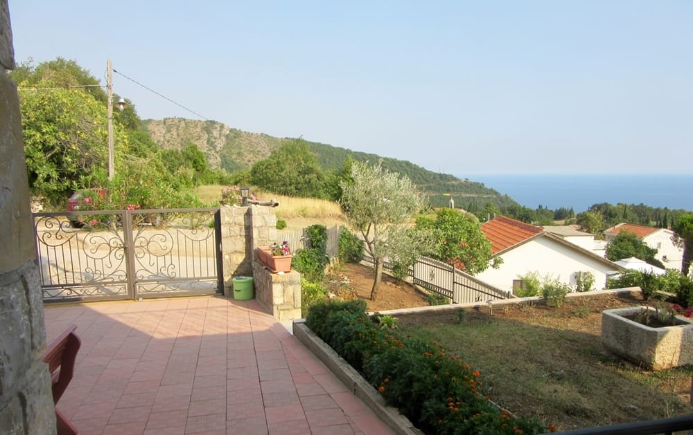 Villa terrace in Rezevici, Montenegro: sea, mountain, and well-kept garden views with an olive tree and stone decor.