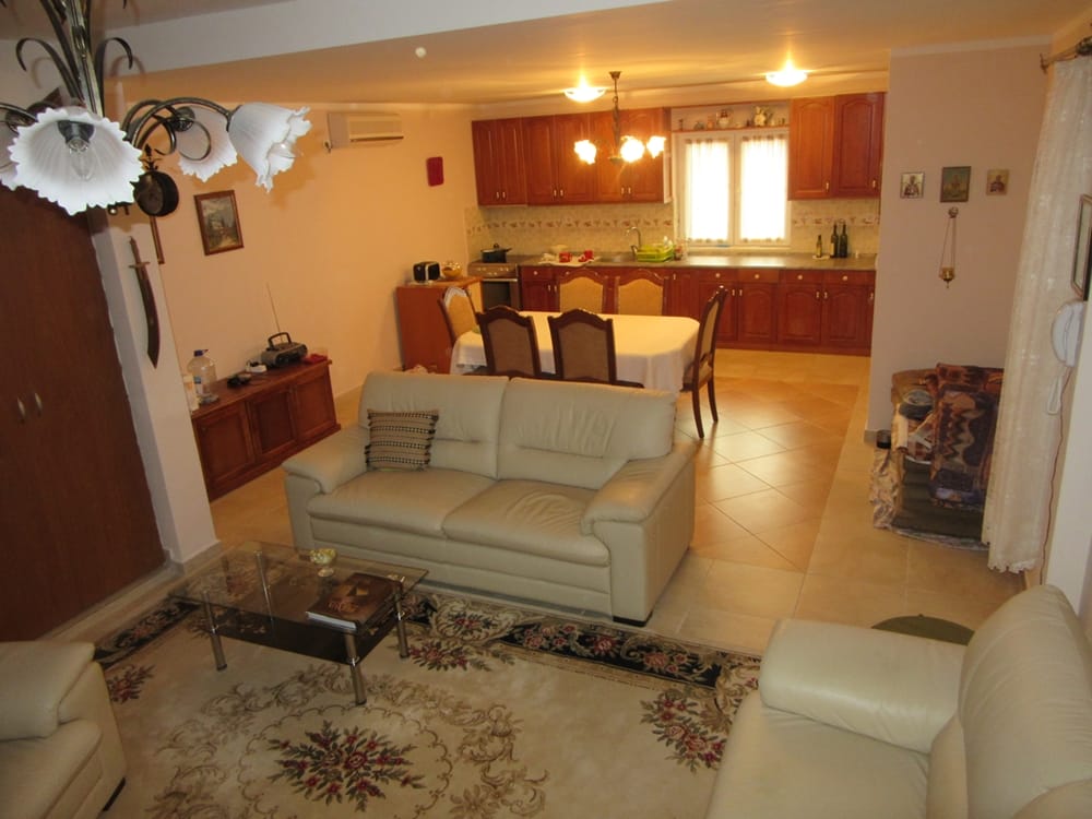 Living room with kitchen in a villa in Reževići, Montenegro: light leather sofas, dining area, and wooden cabinetry.