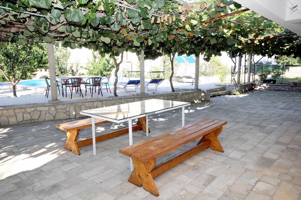 House terrace in Reževići, Montenegro: stone floor, wooden benches, grapevine canopy, and a view of the pool.
