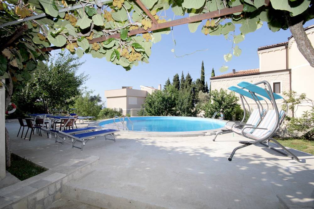 Outdoor pool with sun loungers and swings in the garden of a house in Reževići, Budva Riviera, Montenegro, under a kiwi vine canopy.