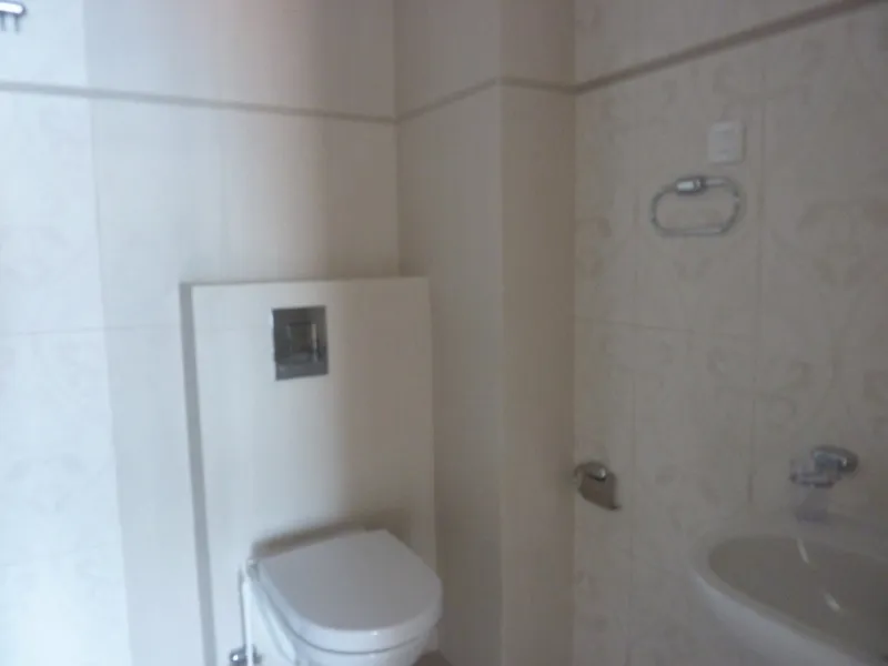 Visible toilet, sink, and towel ring on light tiled walls with floral patterns.