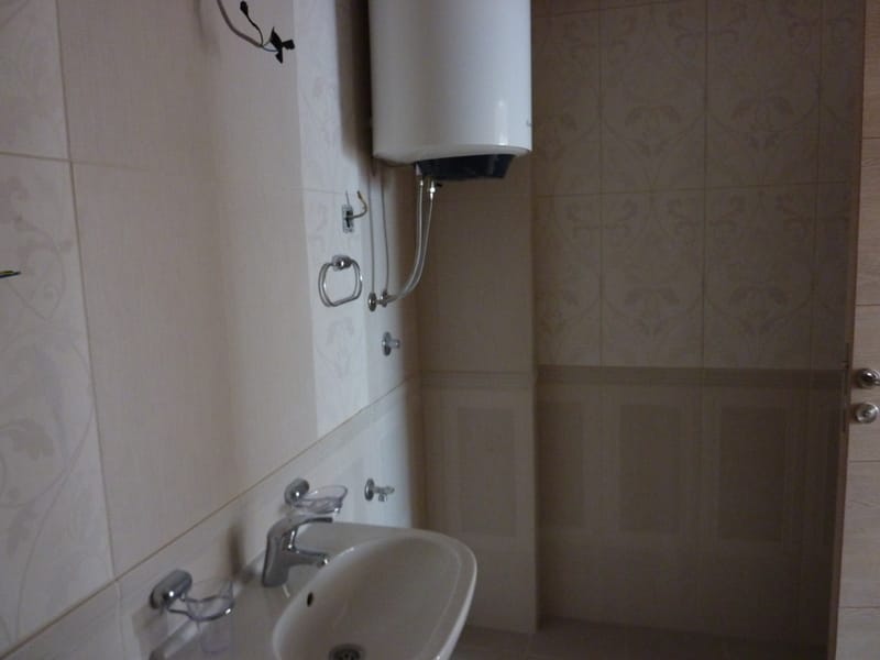 Bathroom in an apartment in Pržno, Montenegro: light tiles, installed water heater, and a sink with faucet.
