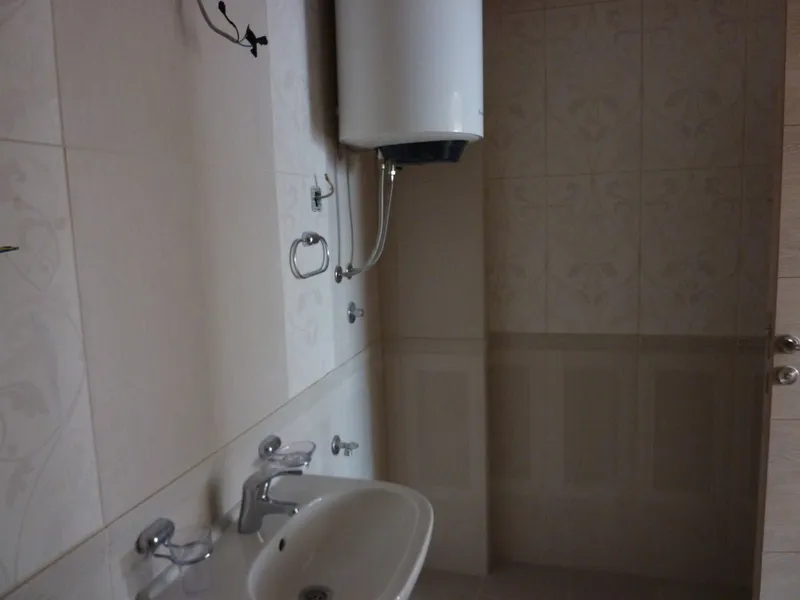 White sink, wall-mounted water heater, patterned tiles on walls, metal towel ring visible in a small bathroom space.