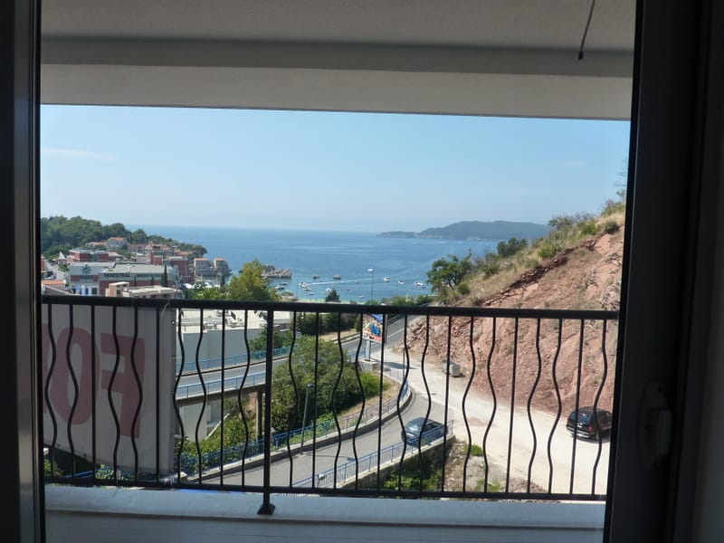 View from the apartment balcony in Pržno, Montenegro: a panorama of the Adriatic Sea, the Maestral Hotel, and mountain scenery.