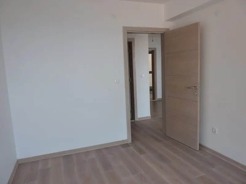 Empty room with white walls and light laminate flooring, featuring an open wooden door leading to a hallway.