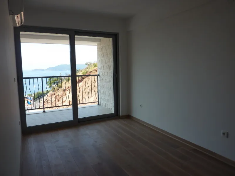 Empty room with laminate flooring and large sliding glass door opening to a balcony overlooking the sea.