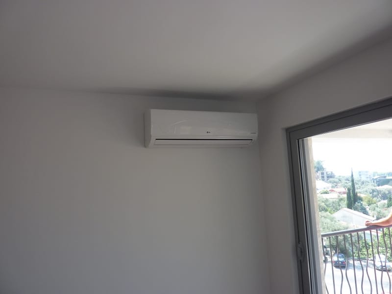 LG air conditioner in a bright apartment living room in Pržno, Montenegro, with access to the balcony and a view of the green landscape.