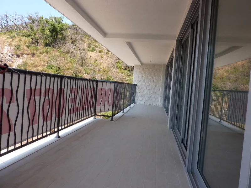 Long balcony with tiled flooring and black metal railing overlooking a dry, grassy hillside.