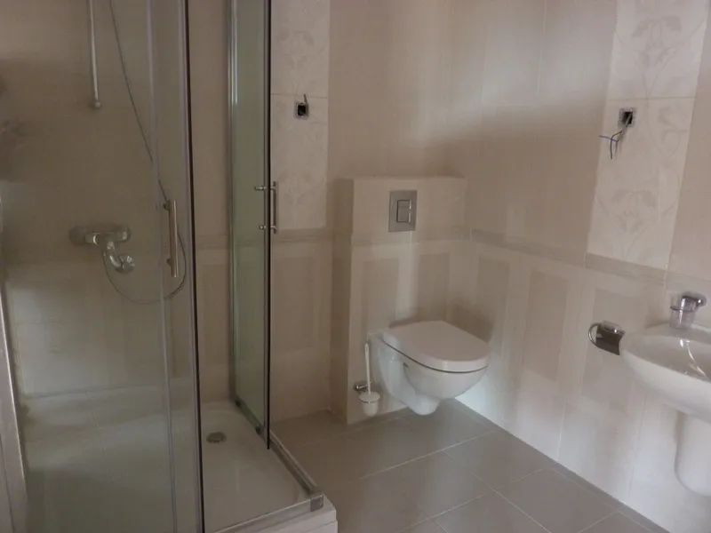 Bathroom featuring a glass shower enclosure, wall-mounted toilet, and pedestal sink with beige tiles.