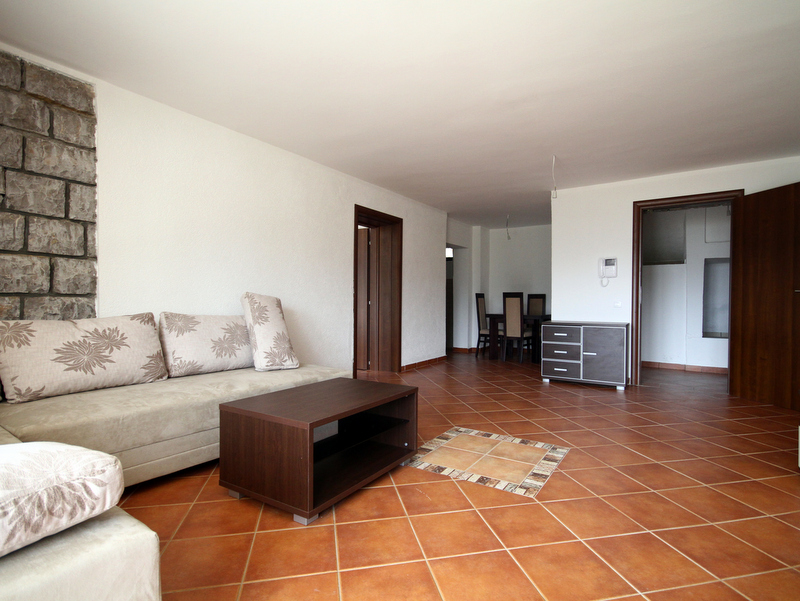 Living room in an apartment in Bečići, Montenegro: a bright room with a stone-accent wall, a soft sofa, and a dining area.