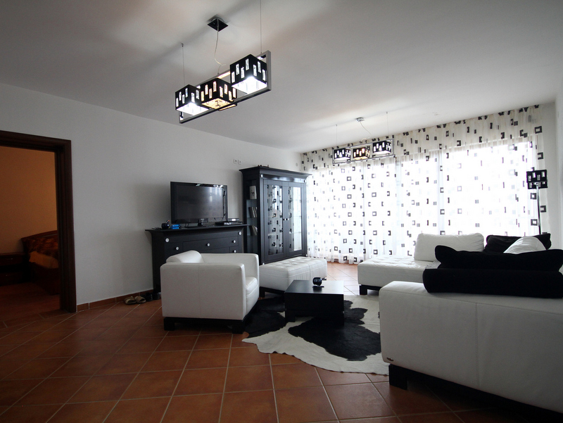 Living room in an apartment in Bečići, Montenegro: white upholstered furniture, a black cabinet, tiled floor, and a zebra-print rug.
