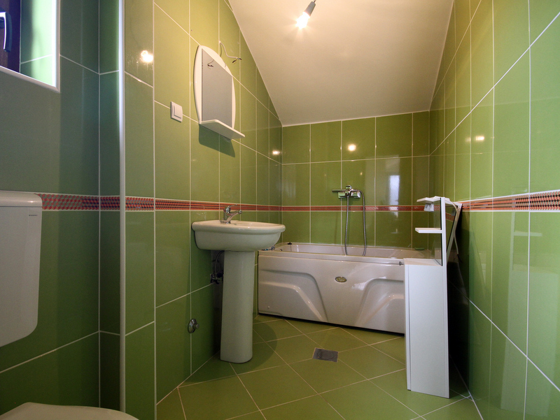 Bathroom in an apartment in Bečići, Montenegro: green tiles, white fixtures, a bathtub, and a mirror in the interior.
