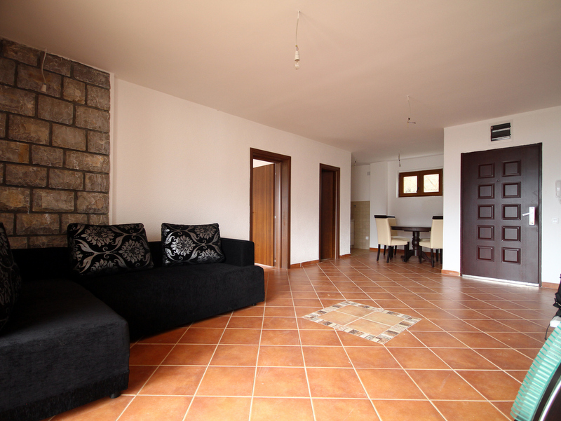 Living room in an apartment in Bečići, Montenegro: black sofa, stone wall, tiled floor, and dining area.