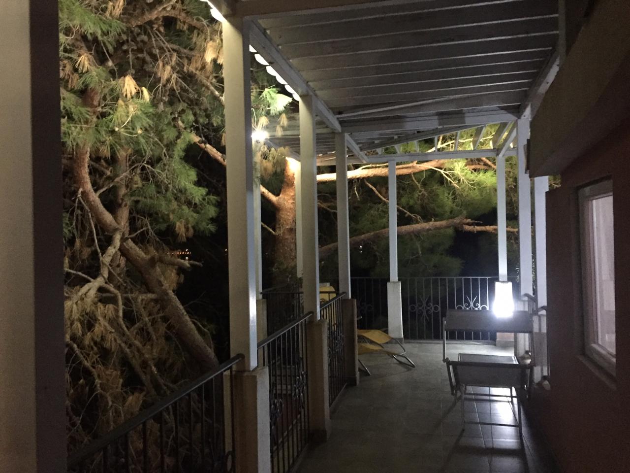 Cozy covered terrace with garden furniture at a house in Shushan, Montenegro, with a view of pine trees in evening light.
